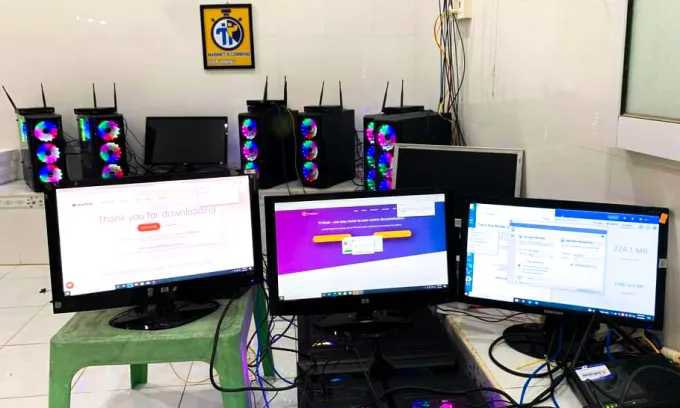 A photo shows three computer monitors on plastic tables, with Pi-themed gaming PCs with RGB-lit fans lined up behind them in what appears to be a technology classroom or node operation setup.