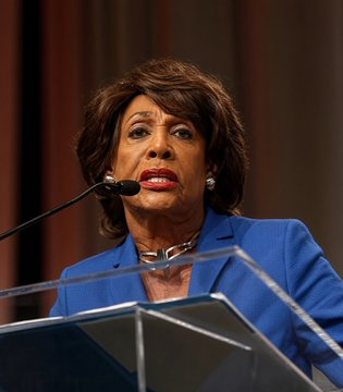 A woman in a blue blazer speaking at a podium with a microphone.