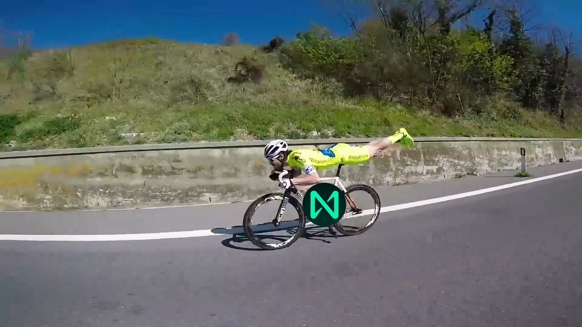 iker in yellow and black suit rides a bicycle with green and white accents, leaning forward on the handlebars against a backdrop of lush greenery and clear blue sky.