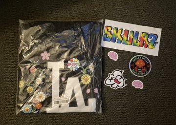 A sealed plastic package containing an 'LA' logo design with floral patterns, alongside stickers featuring 'SKULZ' in rainbow lettering and a Jack Skellington illustration.