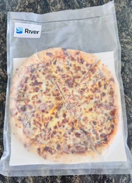 The image features a pizza sitting inside of a clear plastic bag that has been sealed with a zipper. The pizza appears to be frozen, as indicated by its placement in the freezer. The background of the image is blurred, drawing attention to the pizza and the plastic bag.