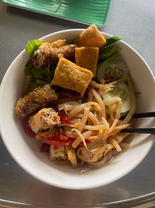 A bowl of Vietnamese noodle salad with crispy spring rolls, fried tofu, and fresh vegetables is served with chopsticks.