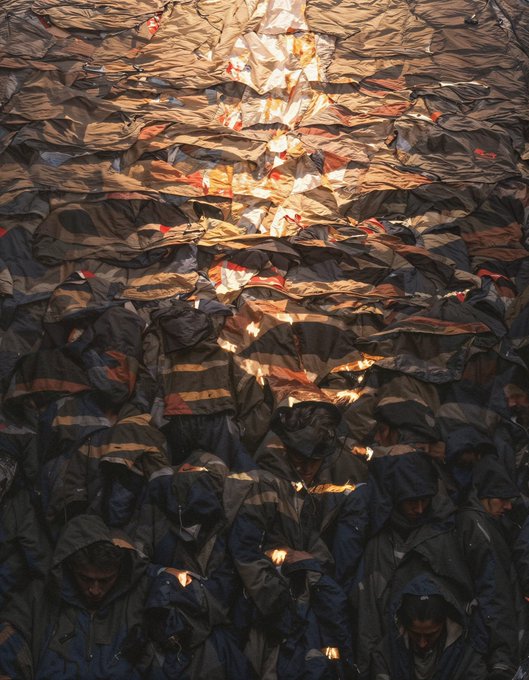 A distorted, repeating visual effect shows a crowd of people wearing dark jackets and hats in what appears to be an outdoor gathering, with the imagery warped into wavy horizontal patterns.