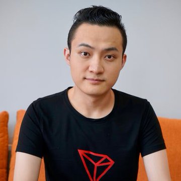 A young man with short dark hair wearing a black t-shirt featuring a red Tron logo, sitting on an orange couch.