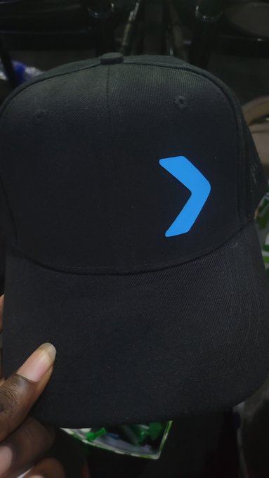 A black baseball cap held by a hand, featuring a glowing blue chevron or arrow symbol on the front panel.