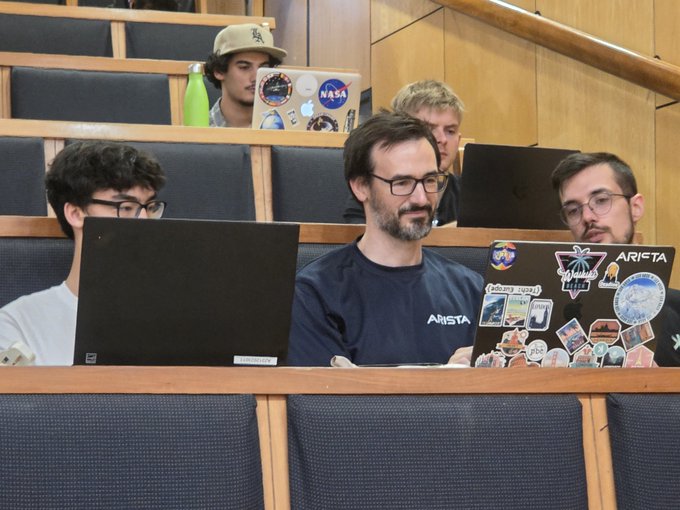 A group of attentive listeners sits in a lecture hall with laptops, one adorned with a prominent NASA sticker and another covered in space and "ARISTA" branded stickers, reflecting the post's mention of a workshop talk about building on $KAS (Kaspa). The focused engagement of the audience suggests genuine interest in the cryptocurrency and blockchain development topics being presented.