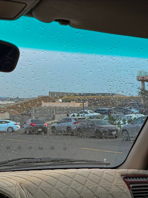 A view from inside a car looking through a rain-covered windshield at a parking lot with several vehicles, including what appears to be a Hyundai.
