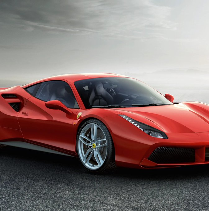 A sleek red Ferrari sports car parked on a road under a cloudy sky.