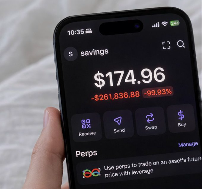 A hand holds a smartphone displaying a crypto savings balance of '$174.96' with a red loss of '-$261,836.88' and a '-99.93%' drop.