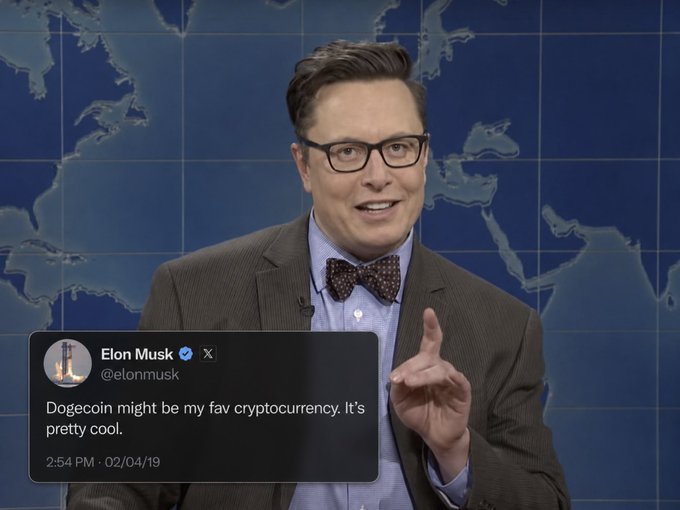 A man wearing glasses and a bow tie stands in front of a world map backdrop, pointing upward while a tweet overlay from Elon Musk (@elonmusk) displays: "Dogecoin might be my fav cryptocurrency. It's pretty cool." posted at 2:54 PM on 02/04/19, visually reinforcing the accompanying post about his endorsement of Dogecoin.