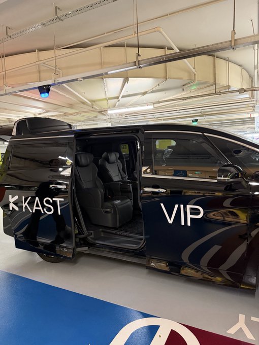 A black VIP van with its sliding door open, revealing luxury captain's chairs inside, parked in an indoor garage with 'KKAST' branding.