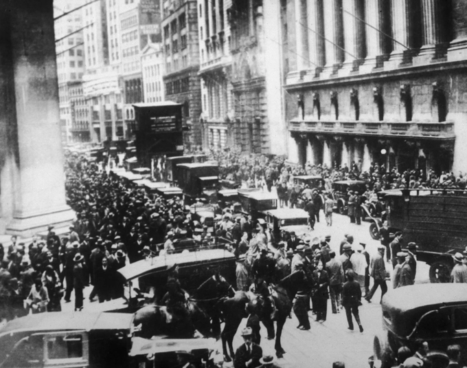 A black-and-white photograph showing a dense, bustling crowd of people, horse-drawn carriages, and early automobiles filling a city street lined with tall buildings, evoking the bustling financial district era before the 1929 stock market crash. The image serves as a visual analogy for the post's warning about modern permissionless tokenized "stocks" that lack real underlying assets, mirroring the speculative fervor of the late 1920s that led to catastrophic losses.