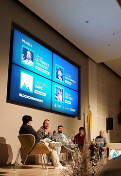 A panel discussion on blockchain takes place on stage, featuring four speakers seated in chairs before a large screen displaying "Panel 3" with the moderator "Dovile Zalkauskaite," panelists "Leonardoy Daio" and "Lucas Martin," and the topic "Blockchain Wars." The Spanish caption confirms the speaker's participation in this blockchain ecosystem panel, where they shared perspectives from AvaLabs on payments and the industry's future.