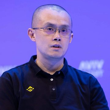 A man with a shaved head and glasses wearing a black polo shirt with a yellow logo speaks against a purple background. The image appears to relate to the accompanying post about Binance founder CZ warning users to diversify their crypto holdings across multiple wallets following the Coldcard security incident.