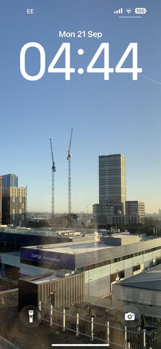 An iPhone lock screen displays the time 04:44 on Monday, 21 Sep, showing a daytime view of a city with construction cranes and buildings.