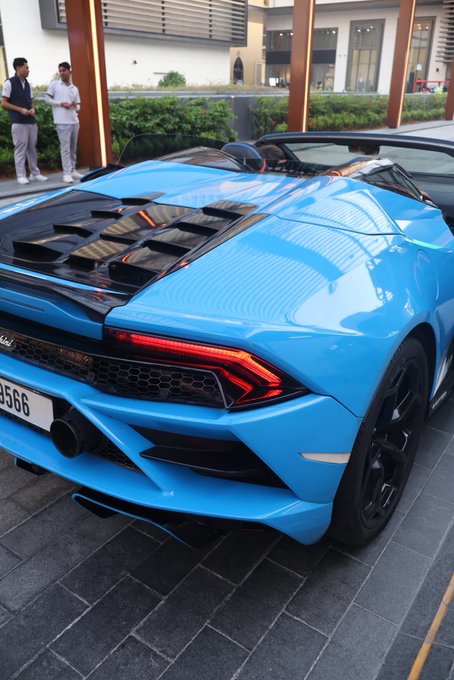 A vibrant blue Lamborghini Huracán Evo Spyder is parked outside what appears to be a luxury hotel or showroom, with a license plate ending in "3566" visible. The "GM (get money)" caption reflects the aspirational status symbol the exotic sports car represents.