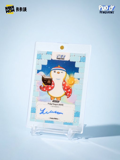 A Pudgy Penguins #0445 autograph collectible card signed by Luca Netz, displayed in a plastic case on a stand.