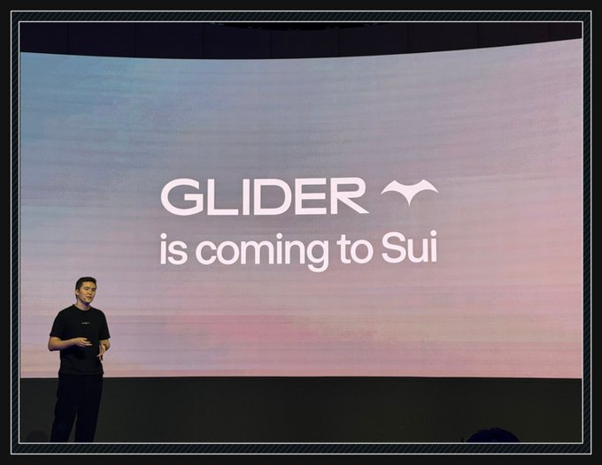 A presenter stands on stage in front of a large screen displaying the text "GLIDER is coming to Sui".