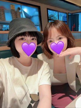 A selfie of two people whose eyes are covered with purple heart emojis; one wears a gray bucket hat and the other makes a heart shape with their arm.