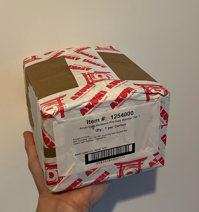 A hand holds a sealed Azuki Galp Awakens Pre-Sale Booster Box (Item #125400) wrapped in branded red and white tape.