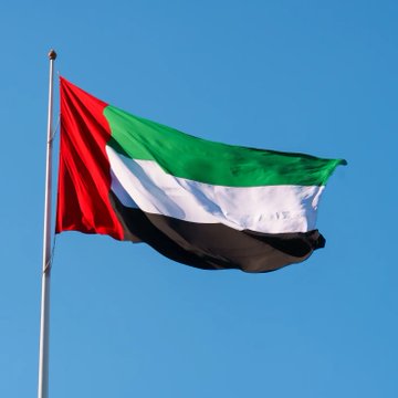 The flag of the United Arab Emirates waves in the wind against a clear blue sky, symbolizing the nation mentioned in the post about the UAE planning to integrate Avalanche ($AVAX) into its national digital identity platform, UAE PASS.