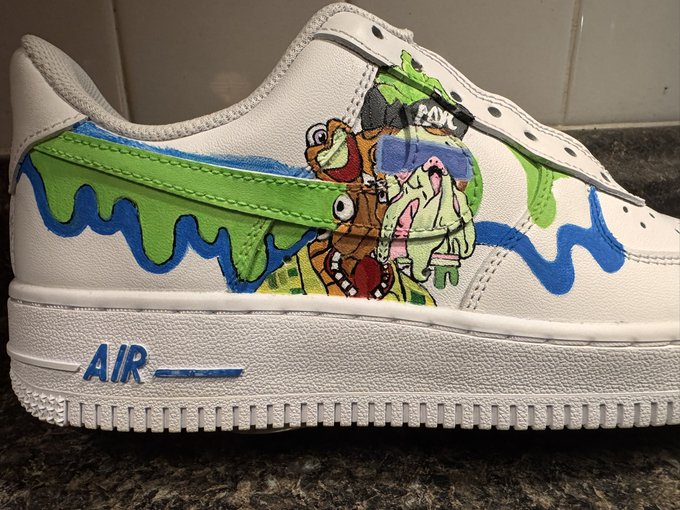 A close-up of a custom white Nike Air Force 1 sneaker featuring hand-painted artwork of SpongeBob, Patrick, and Squidward with green slime drips and blue paint accents.
