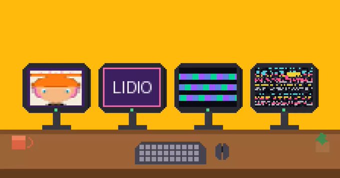 Pixel art of a desk with four monitors displaying various images including a character face, 'LIDIO' text, and glitch patterns, along with a keyboard and mouse.