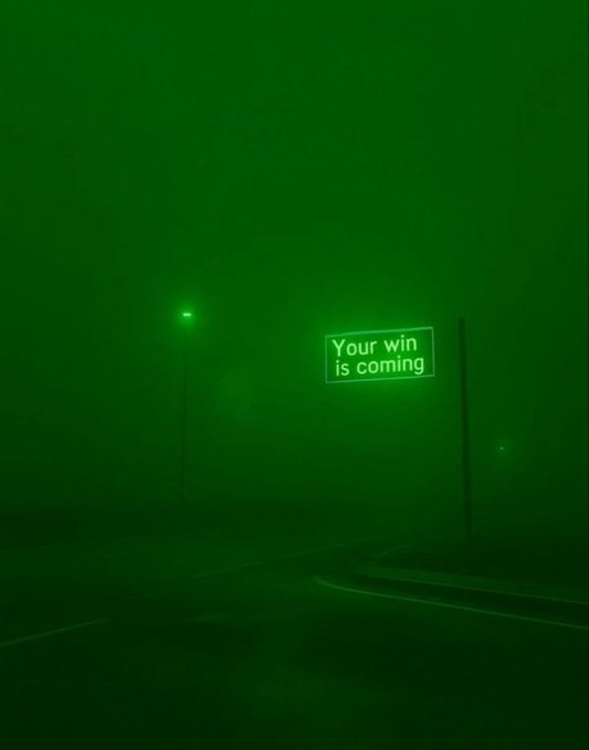 A green night vision-style image captures a road sign illuminated in the dark that reads "Your win is coming," creating an eerie, monochromatic scene with a streetlamp glowing nearby.