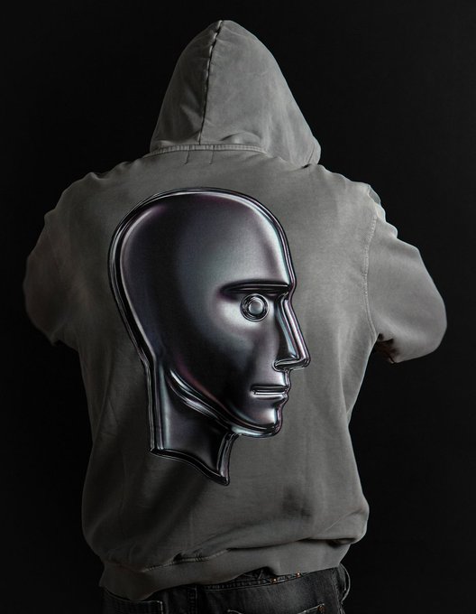 A person seen from behind wears a gray hoodie with a large metallic sculptural head design on the back.