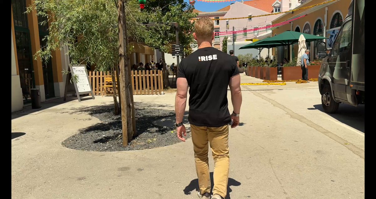 The image shows a man walking down an empty street, wearing a black shirt with white text that says "Tribe". The surrounding area appears to be a plaza or courtyard with trees and buildings nearby. There are also people present in the scene, but they seem to be further away from the main subject of the photo.

The post features a question about an upcoming event at the Basel Art Summit, asking if anyone has seen this good vibe video from @NFCsummit that includes the image of the man walking down the street with "Tribe" written on his shirt. The caption suggests that the artist might be interested in collaborating or showcasing their work at the summit.