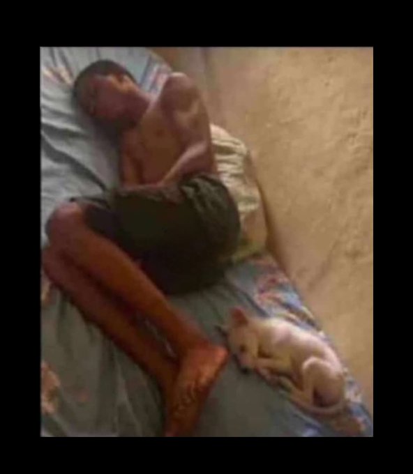 A grainy photograph showing an elderly person lying on a mattress on the floor next to a small white dog, with the person appearing emaciated and the setting looking impoverished.