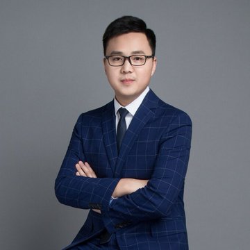 A professional headshot of an Asian man wearing glasses, a blue checkered suit, and a dark tie, standing with his arms crossed against a grey background.