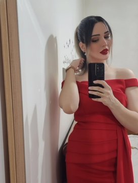 A woman in an elegant red off-the-shoulder dress takes a mirror selfie, holding a smartphone while posing in what appears to be a hallway. The polished, glamorous aesthetic of the portrait aligns with the post's reference to an art profile, suggesting the image may represent the artistic identity or persona associated with the referenced objkt.com token link.