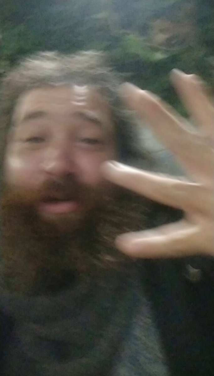 The image features a man with a beard, wearing a scarf around his neck, making a peace sign by raising one finger while holding out another. The caption below the photo reads "Easy instructions on how to do the Kaspa hand sign". This suggests that the image is promoting the Kaspa hand sign as an easy and fun way for people to learn about Bitcoin or cryptocurrency.