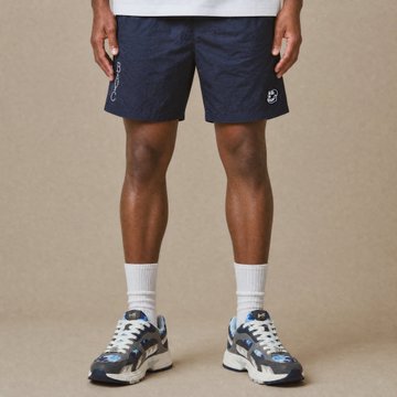 A person models navy blue athletic shorts paired with white socks and chunky blue-and-white sneakers against a beige background.