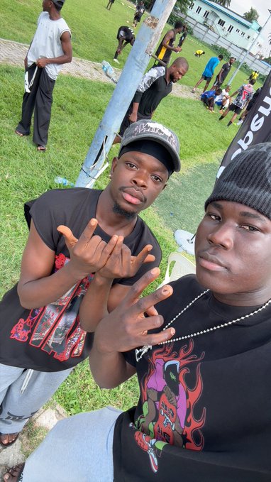 Two friends, identified as "web2 mutuals," pose for a selfie at an outdoor event where other people are visible in the background.