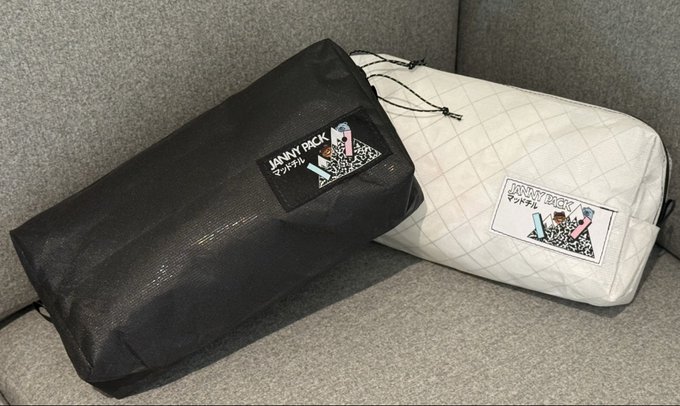 Two 'JIMMY PACK' drawstring bags, one black and one white, resting on a gray couch.