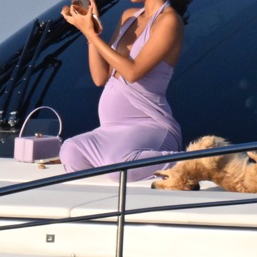 A pregnant woman in a lavender dress sits on a yacht holding a phone, accompanied by a small dog resting nearby. The "LEO" caption likely refers to a zodiac sign or name, complementing the relaxed, sunlit scene of leisure and elegance.
