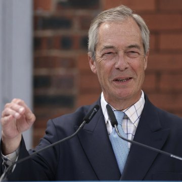 Nigel Farage, the leader of Reform UK, speaks into a microphone during a public appearance. His poised gesture and serious expression suggest he is addressing a contentious topic, aligning with the post about his announcement to resign as MP amid ongoing parliamentary investigations into crypto-linked donations.