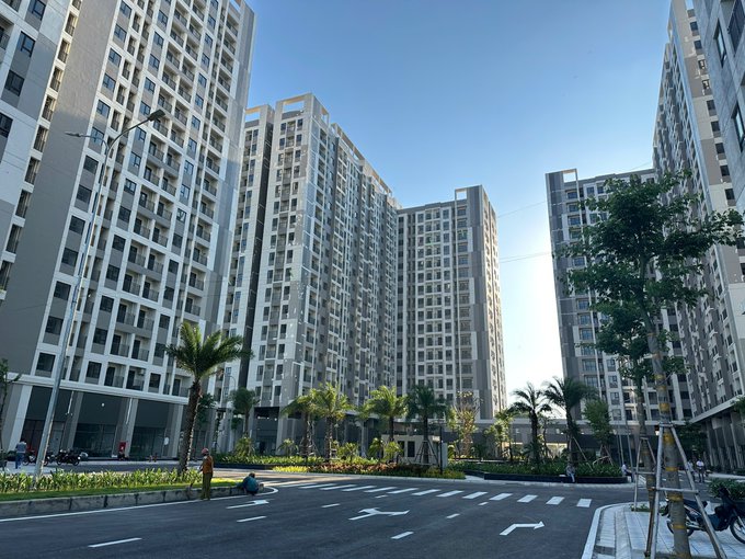 A view of a modern residential complex with several tall apartment buildings, palm trees lining a street, and a clear blue sky.