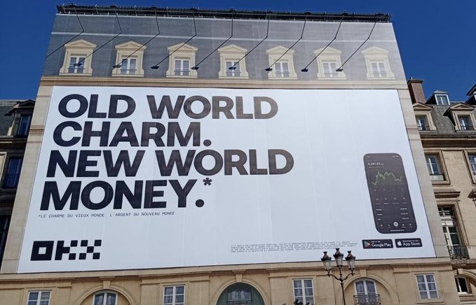A billboard on a building reads 'OLD WORLD CHARM. NEW WORLD MONEY.' for OKX, with a French translation 'LE CHARME DU VIEUX MONDE. L'ARGENT DU NOUVEAU MONDE' and an image of the OKX app.