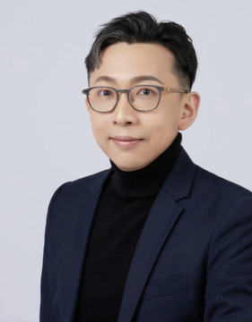 A professional headshot of a man with short black hair and glasses, wearing a black turtleneck under a dark blazer against a light gray background, presented as a portrait accompanying a news report featuring Taiwan lawmaker Dr. Ko Ju-chun discussing the likelihood of Taiwan establishing a strategic Bitcoin reserve.