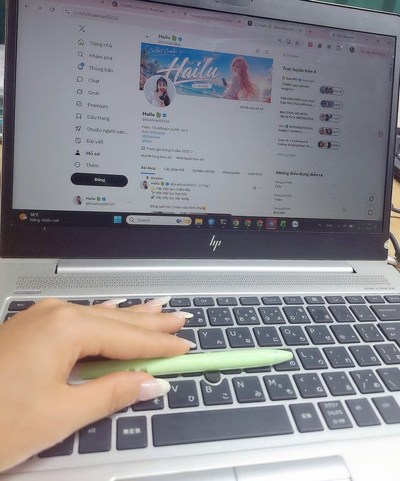 A close-up photo shows a person's hand with long manicured nails resting on the keyboard of an HP laptop, holding a light green stylus or pen. The screen displays the X (formerly Twitter) profile page for a user named 'Hailu' (@hailubeauty22) with a beach-themed banner.