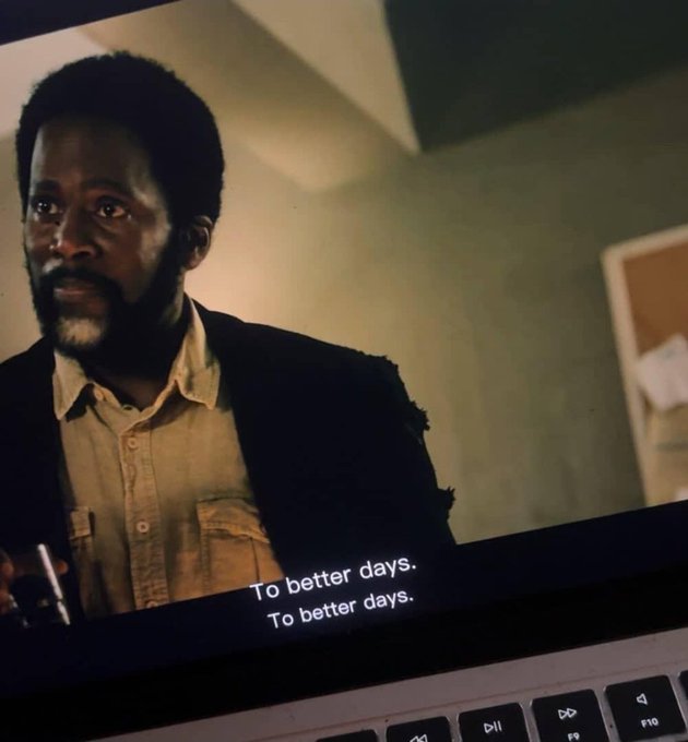 A close-up of a laptop screen displaying a scene with a bearded man and the subtitles 'To better days. To better days.'