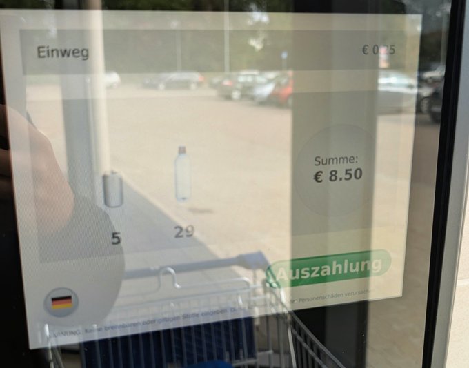 A photograph of a German bottle return machine screen showing 'Summe: € 8.50' with an 'Auszahlung' (payout) button, displaying a 'Einweg' deposit of €0.25, with a parking lot visible through the reflection on the screen.