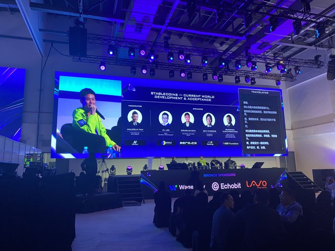 A photo taken at a conference showing a large screen displaying "STABLECOINS - CURRENT WORLD DEVELOPMENT & ACCEPTANCE" with speakers including Philipp Von and others, and "Token 2049" branding visible.