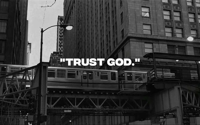 Black and white photograph of a city elevated train passing between buildings, with the text overlay 'TRUST GOD.'