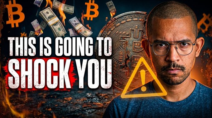 The image features a man with glasses wearing a blue shirt, who appears to be upset or angry. The background of the image shows an explosion of money falling from the sky, which could represent Bitcoin or other cryptocurrencies. The text "This is going to shock you" is written in white above the explosion, and there's also a warning sign that reads "SHOCK YOU".