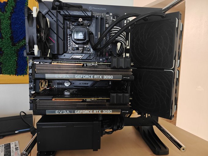 An open Thermaltake computer case on a desk displaying internal components including a CPU water cooling block and two EVGA GeForce RTX 3090 FTW3 graphics cards stacked vertically.