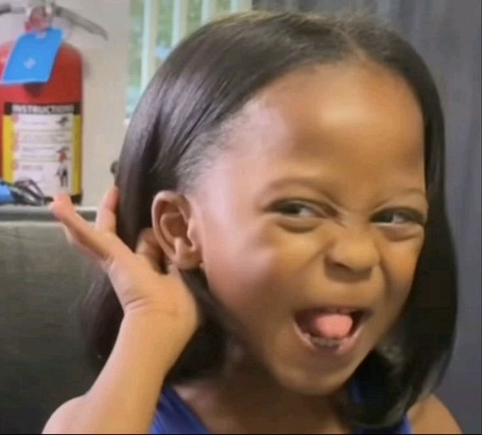A young girl makes an exaggerated, mischievous face while pulling her ear and sticking her tongue out.